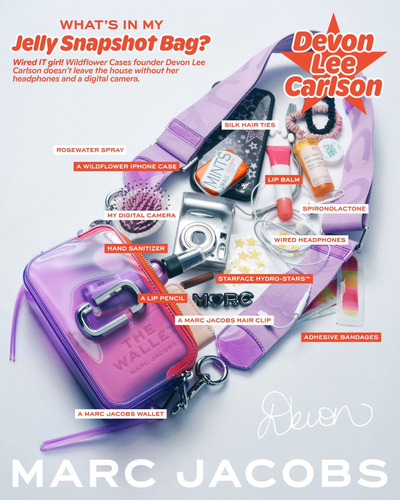 An overhead product shot displays the contents of a Marc Jacobs Jelly Snapshot Bag, including makeup, camera, phone, and accessories.