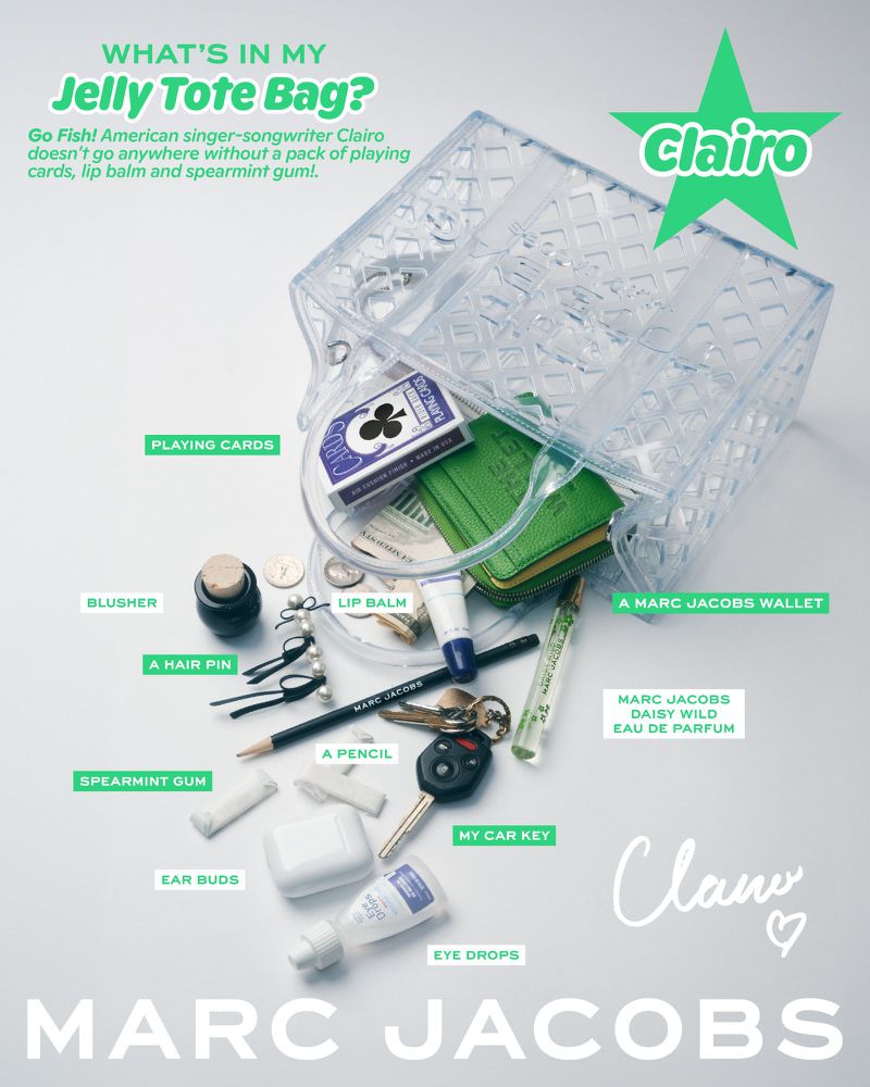Overhead shot of a transparent tote bag with everyday carry items like a wallet, keys, and makeup against a white backdrop.