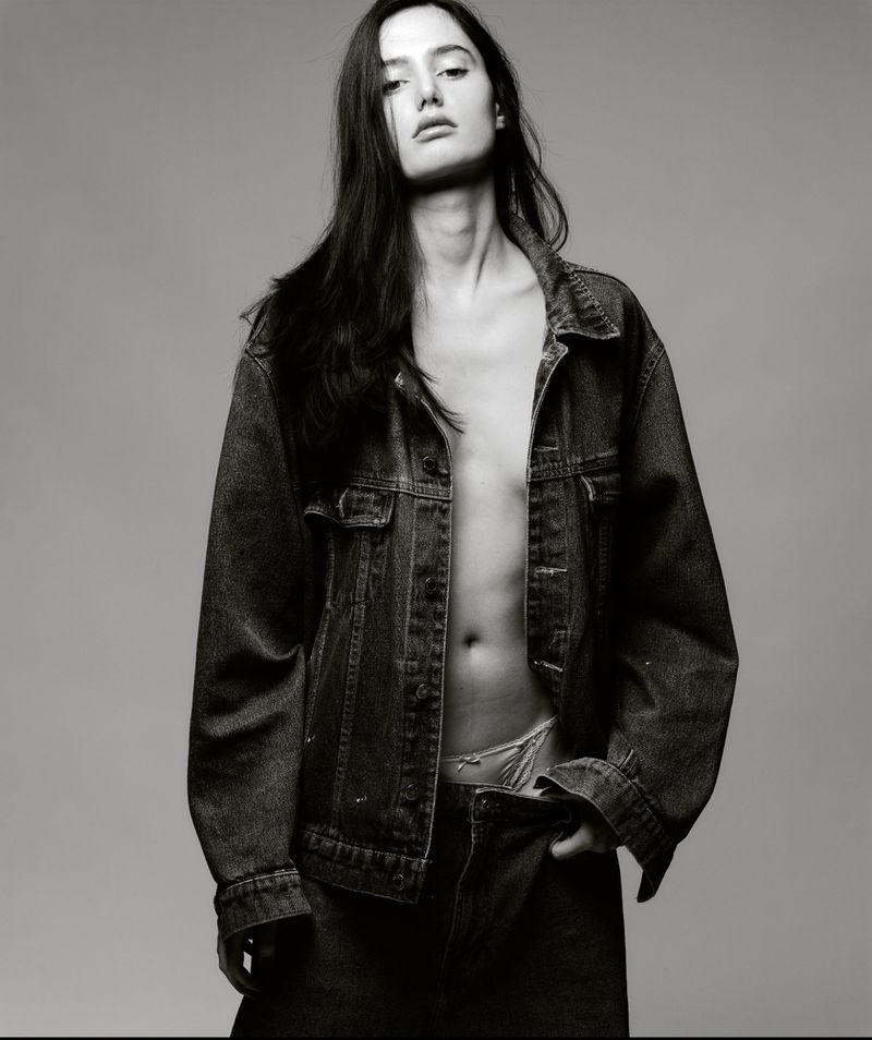 Monochrome portrait of a woman in a denim jacket, looking at the camera with a serious expression in a photo studio.