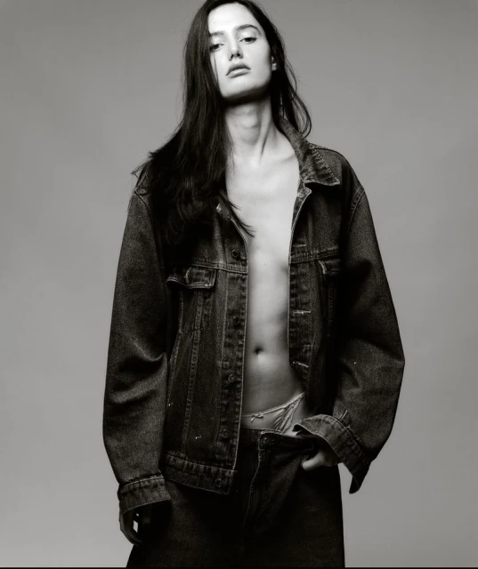 Monochrome portrait of a woman in a denim jacket, looking at the camera with a serious expression in a photo studio.