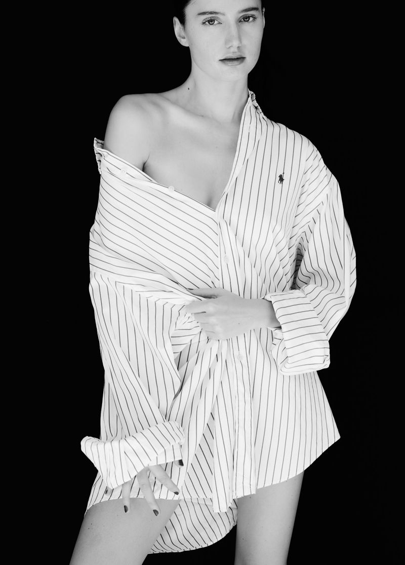 Monochrome portrait of a young woman in an unbuttoned, vertically striped shirt against a stark black background, showcasing fashion.