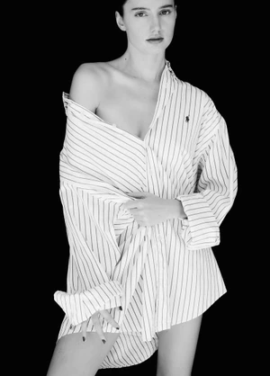 Black and white portrait of a woman wearing an oversized striped button-down shirt against a dark background.