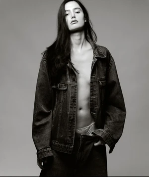 Model Erika Emaldi wearing an unbuttoned denim jacket in a monochrome studio portrait against a plain grey background