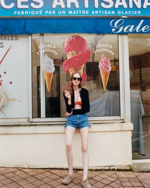 Young woman in casual summer outfit standing in front of ice cream shop window with cone posters.  Fashion, style, sunny, outdoors.