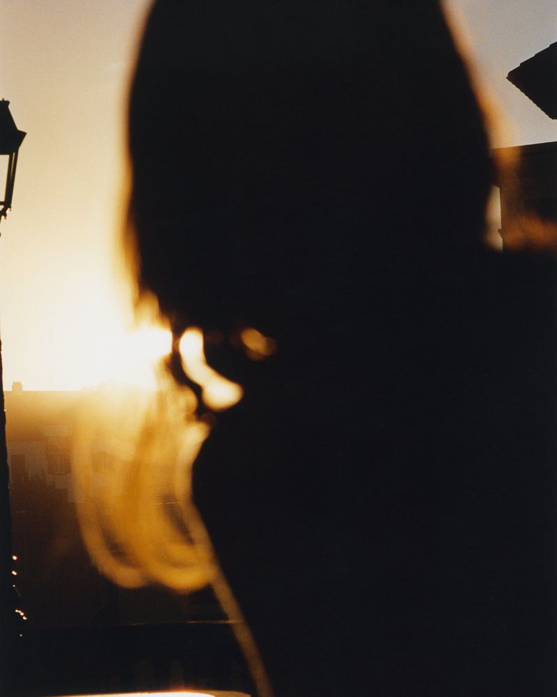 Silhouette of a person with golden blonde hair during sunset, with a vintage lamp post in the background.
