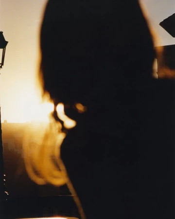 Silhouette of a person with golden blonde hair during sunset, with a vintage lamp post in the background.