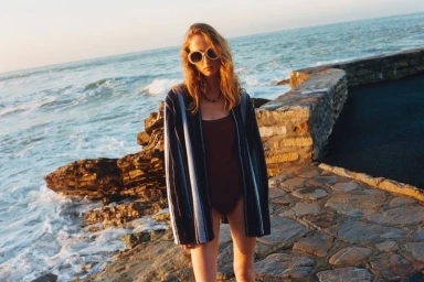 Model wearing sunglasses and striped cardigan by the rocky coast with ocean waves