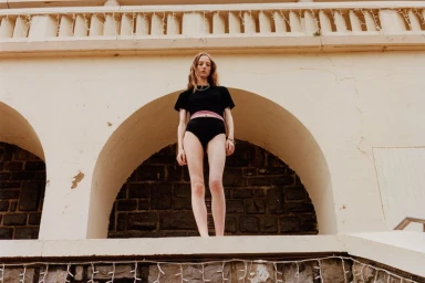 Model standing beneath a stone archway wearing a black top and shorts for Guest in Residence in Biarritz