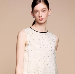 Model Eniko Sipos wearing a cream sleeveless patterned top with dark earrings against a neutral studio background