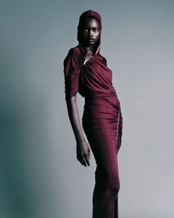Model in a burgundy hooded dress with a zippered neckline posing against a seamless grey studio background