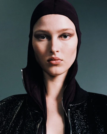 Close-up portrait of a model wearing a dark hooded top and a glittering jacket against a neutral studio background