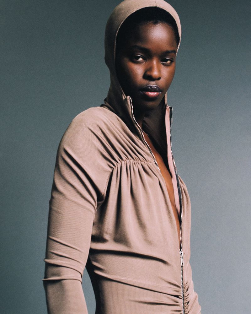 Close-up of a Black female model wearing a light brown, hooded dress with long sleeves, posing in a studio setting with neutral lighting.