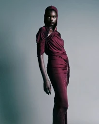 Model in a burgundy hooded dress with a zippered neckline posing against a seamless grey studio background