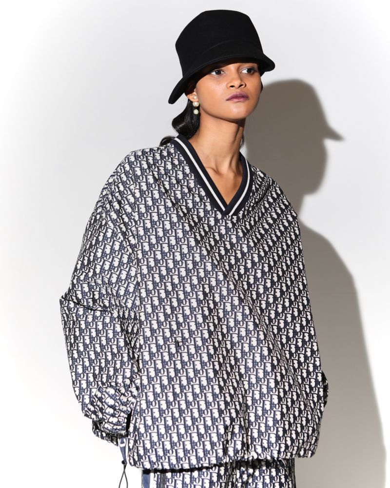 A woman models a patterned jacket and bucket hat in a studio setting, standing against a white backdrop with soft, diffused lighting.