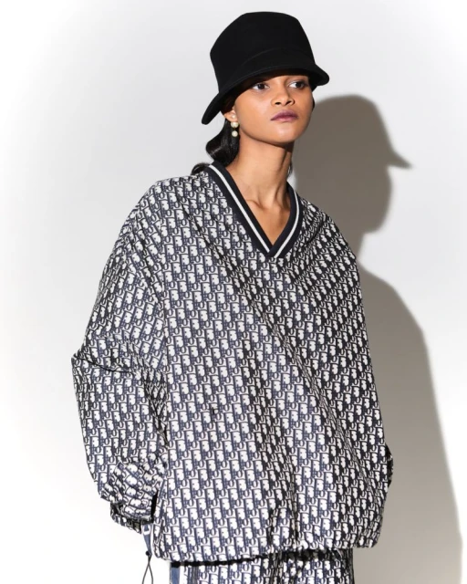 A woman models a patterned jacket and bucket hat in a studio setting, standing against a white backdrop with soft, diffused lighting.