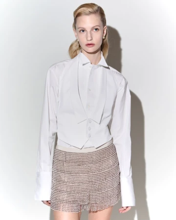 Woman poses in a white shirt and embellished fringe mini skirt against a white backdrop in a fashion studio shot with bright, even lighting.