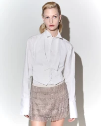 Model in white collared shirt and embellished fringe shorts standing against a bright white studio backdrop