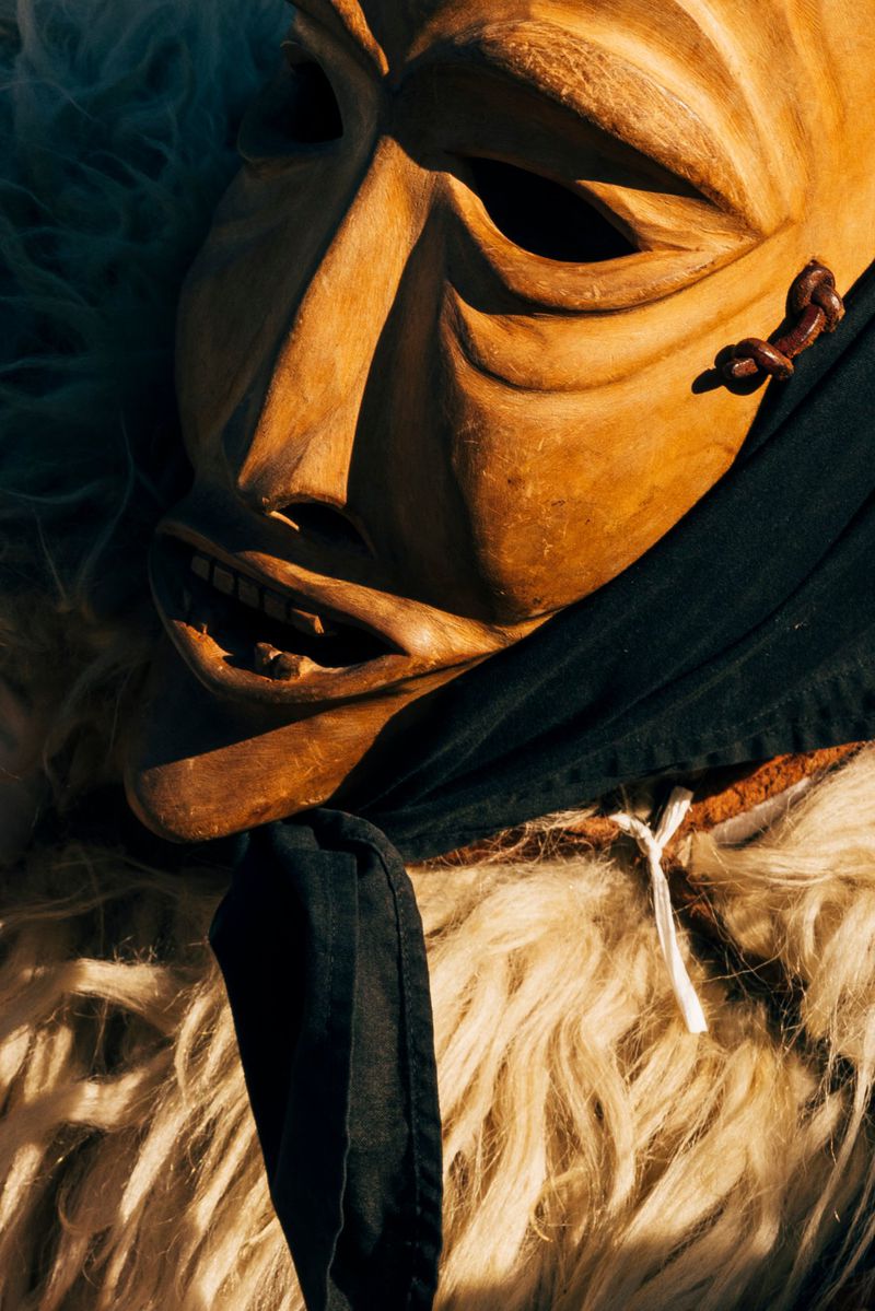 Close-up of a wooden mask with a solemn expression, set against a backdrop of furry fabric and a dark cloth, creating a mysterious feel.