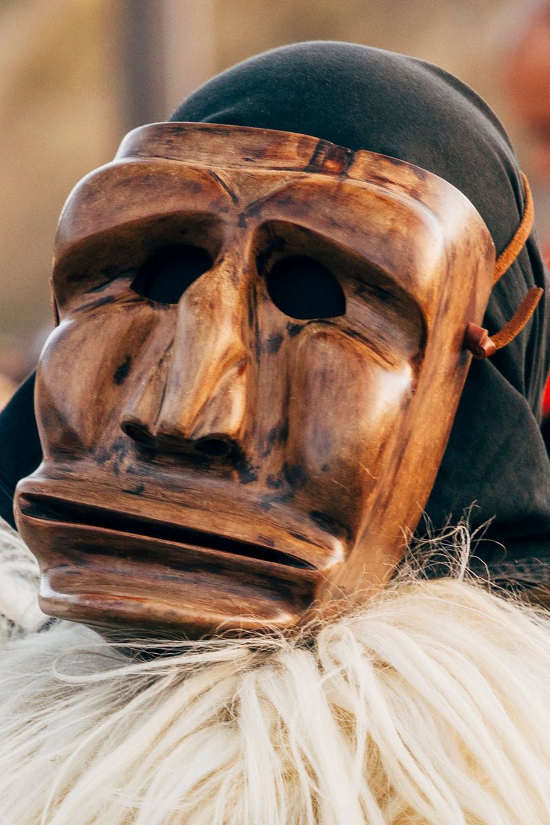 Close-up of a wooden mask with exaggerated features, worn with a dark hood and a white, fluffy collar. Mysterious and traditional.