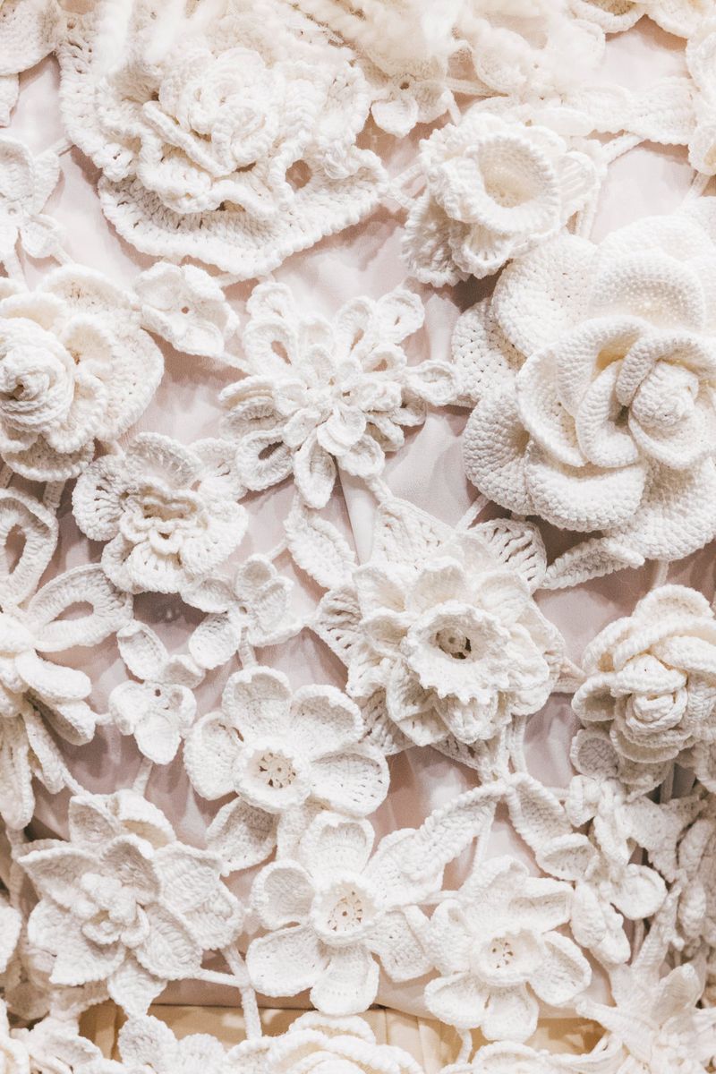 Close-up of an elegant off-white dress with floral patterns. Floral fabric patterns with crocheted flowers on a flowing wedding gown.
