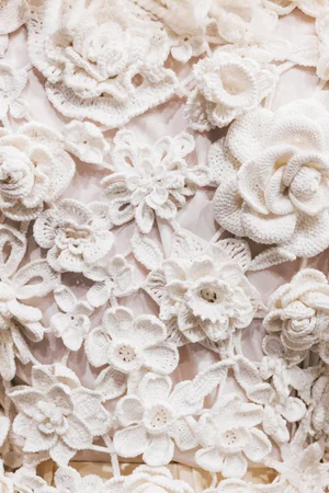 Close-up detail of intricate white crochet floral lace appliques on a garment from Dolce and Gabbana Alta Sartoria.