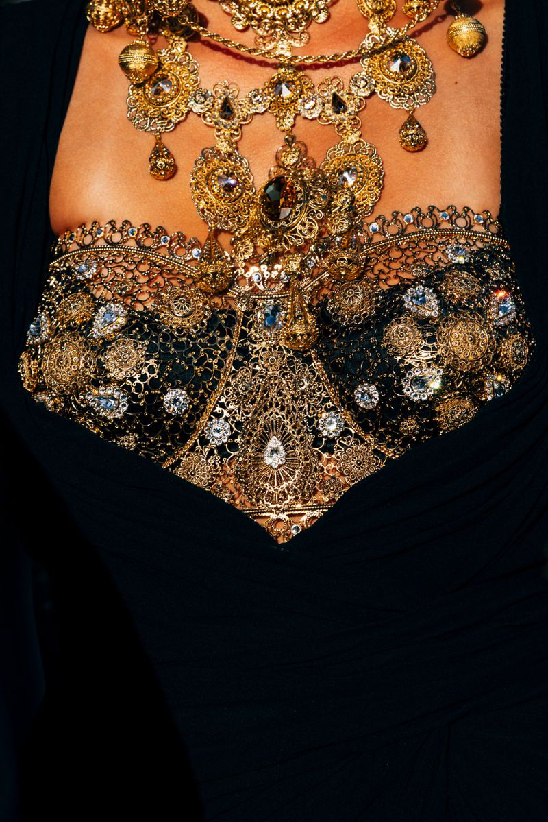 Close-up shot of an adult female's upper body adorned with intricate gold jewelry, gemstones, and a decorative black and gold top.