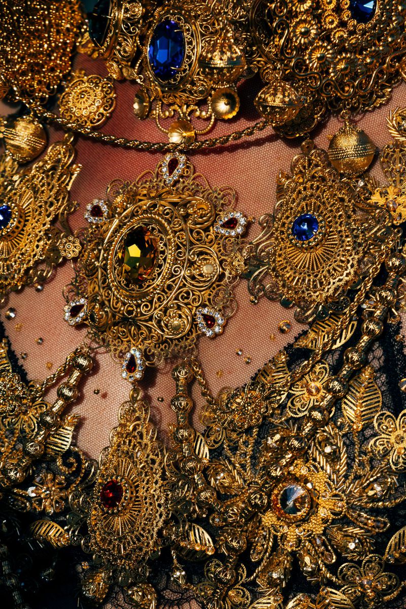 Close-up of ornate gold jewelry with embedded colored gems adorning clothing, highlighting fashion and detailed craftsmanship.