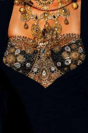 Close-up of a model wearing ornate gold filigree necklaces and an intricate black lace bodice encrusted with sparkling crystals.