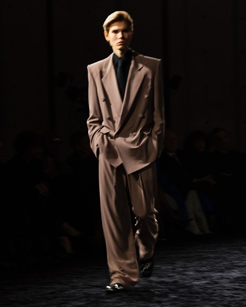 Male model walking the runway wearing a taupe oversized double-breasted suit and dark shirt for Saint Laurent