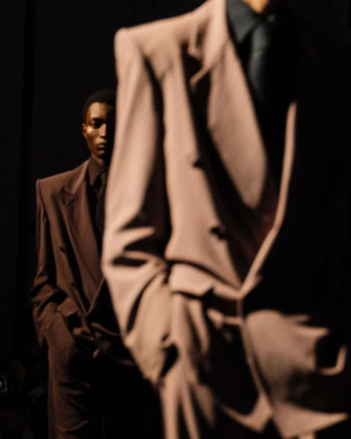 Two African American men in oversized suits in a dark setting, fashion photography. Brown suit jacket, dress shirt and tie.