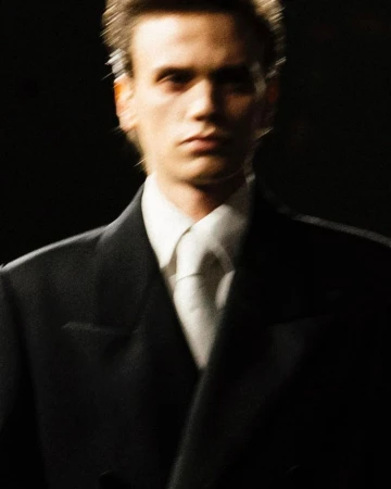 Motion blurred portrait of a male model wearing a black suit and white tie for Saint Laurent