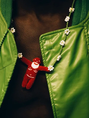 Close-up of a person wearing a vibrant green jacket and a beaded necklace featuring white daisies and a red figurine.
