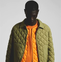 Model wearing an olive green quilted jacket over an orange top against a plain light background for K-Way