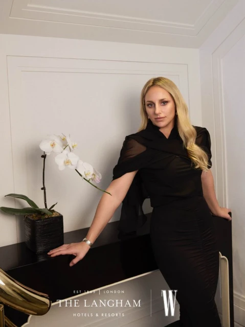 Blond woman in black dress poses next to white orchid in modern interior, logo of The Langham Hotels & Resorts at bottom left.