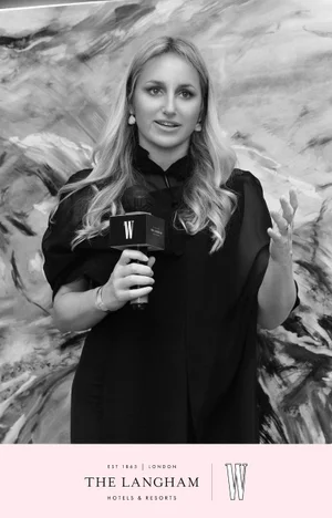 Woman holding a branded microphone in a black dress against an abstract patterned background