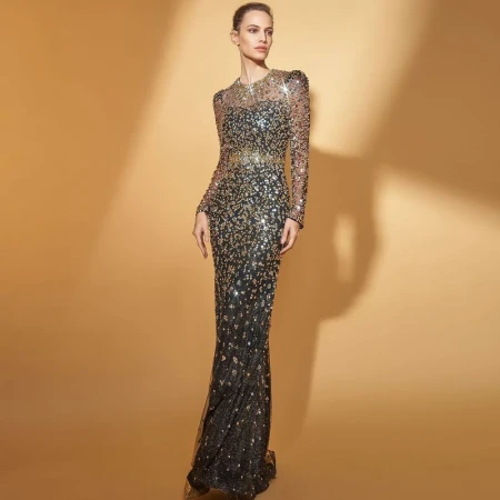 A slender woman poses in a shimmering black and gold sequined gown against a warm beige backdrop in a fashion editorial shot.