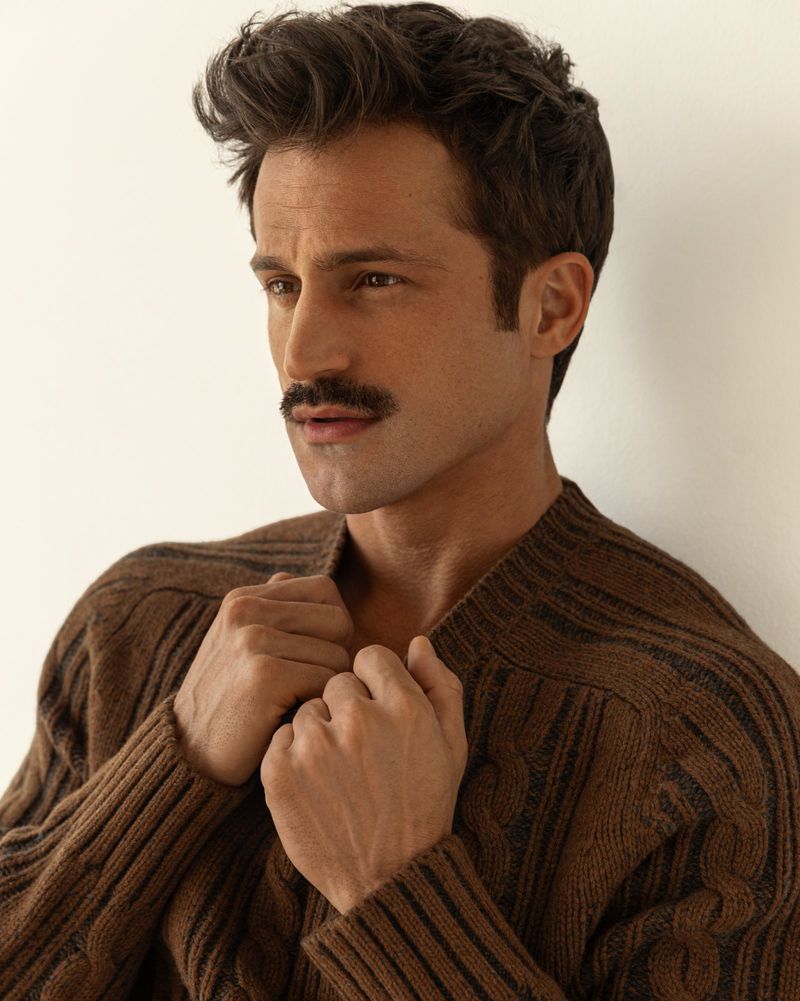 Portrait of adult man with mustache, wearing brown cable knit sweater against neutral backdrop in a studio. Fashion and lifestyle.