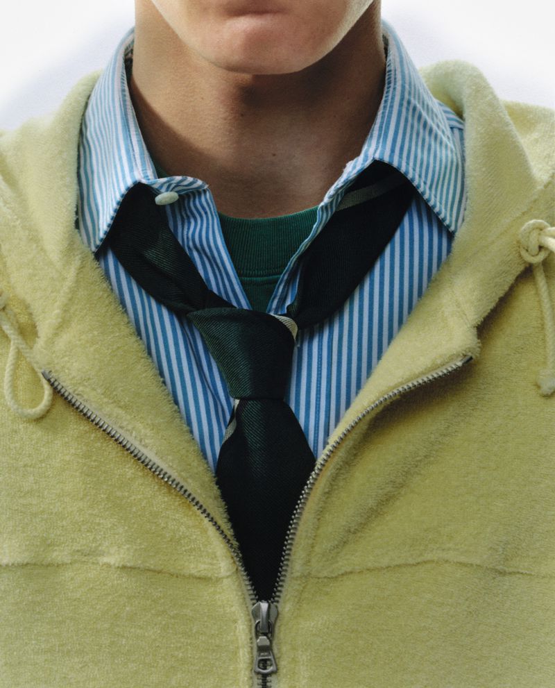 Close-up of a person wearing a green tie, striped shirt, and a yellow jacket, showcasing fashion and style details.