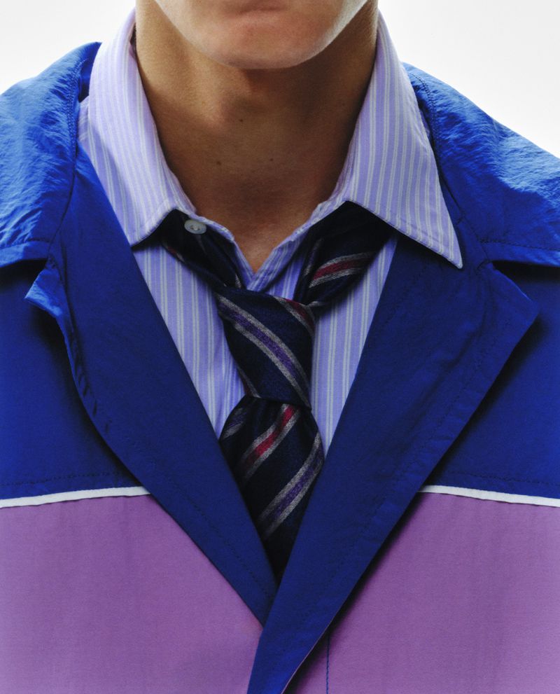 Close-up of a fair-skinned male torso wearing a striped blue and white dress shirt, patterned tie, and blue and purple jacket.
