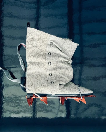 Close-up studio shot of a white mountaineering boot with crampons, featuring a laced design and rugged construction against dark background.