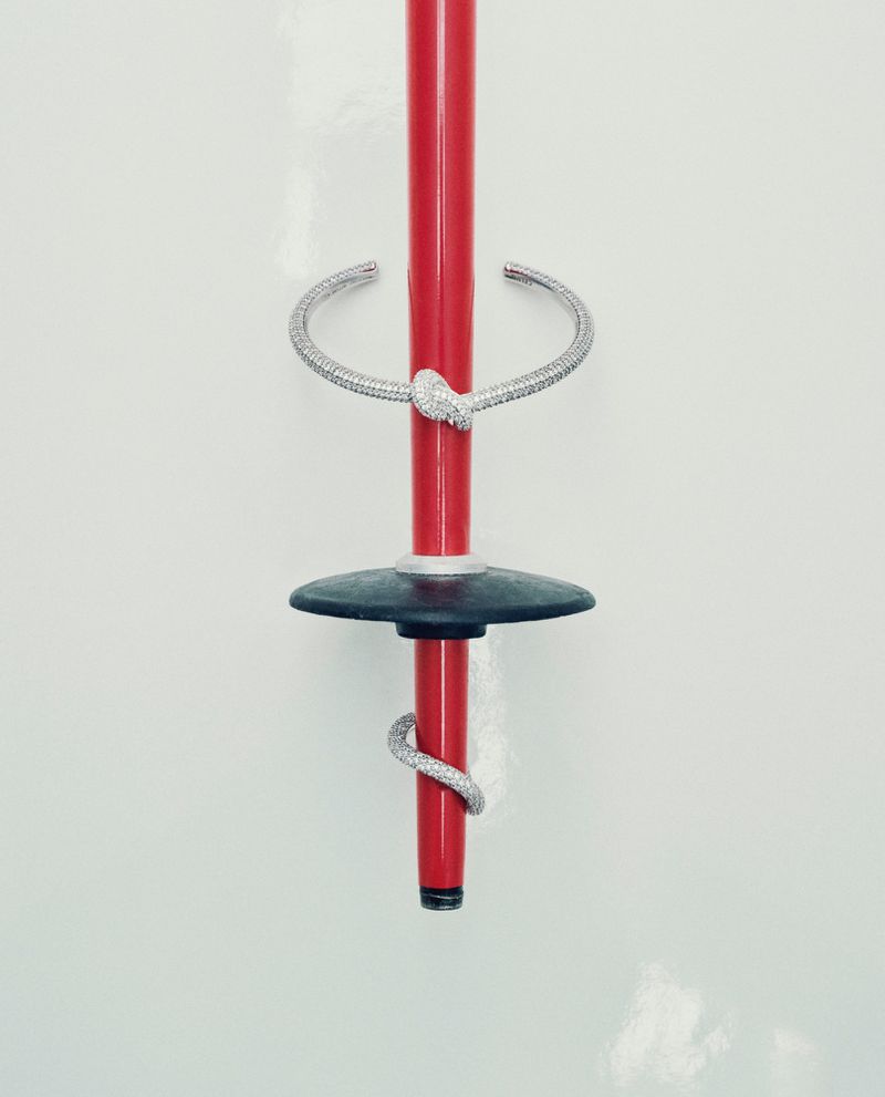 A red ski pole with a snake-shaped bracelet wrapped around it sits against a white background, a stylish and minimalist composition.