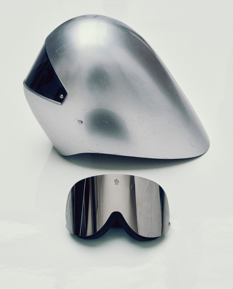 Silver ski helmet and reflective goggles sit on a white surface, capturing a sleek and futuristic aesthetic for winter sports.