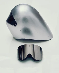 Futuristic silver aerodynamic ski helmet positioned above mirrored ski goggles on a clean white surface.