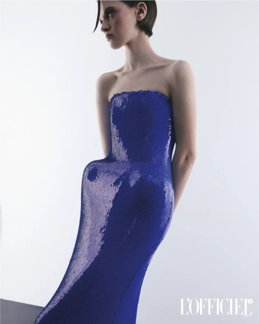 Elegant woman poses in a shimmering strapless gown against a bright white background in a fashion editorial style shot.