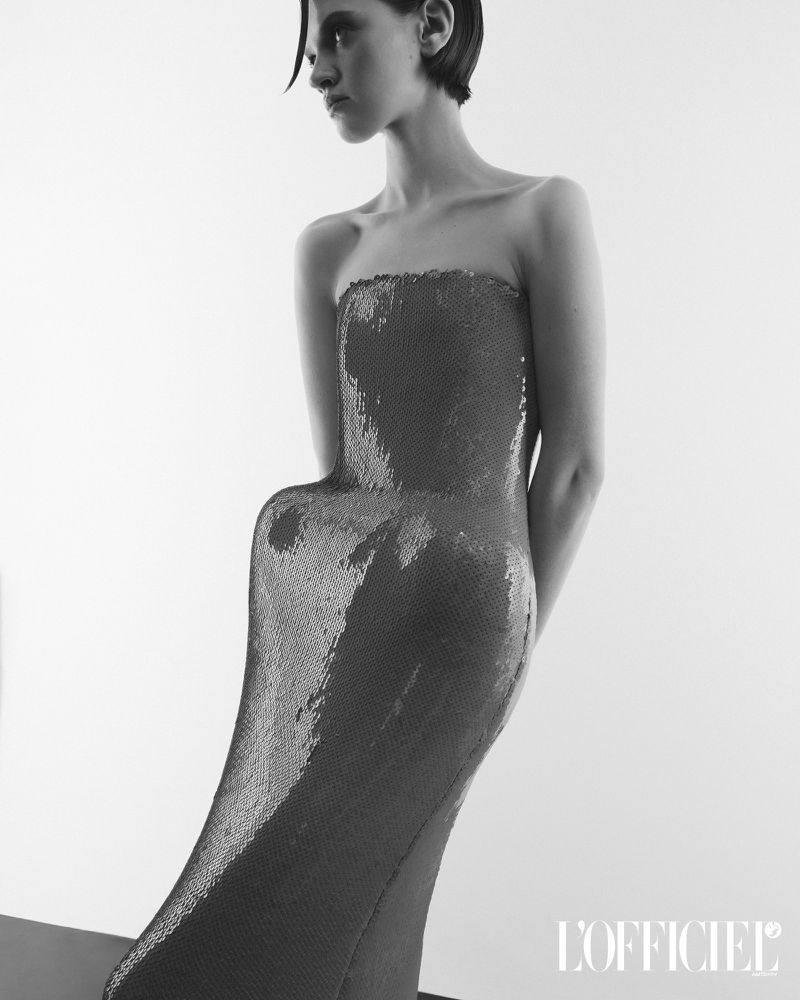Model wearing a strapless sculpted sequin dress against a seamless white studio background for L'Officiel USA
