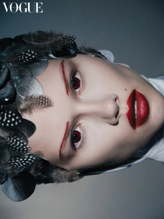 Fashion portrait of a woman with red lips, brows, and eye accents wearing a feather headpiece in a high fashion editorial style.