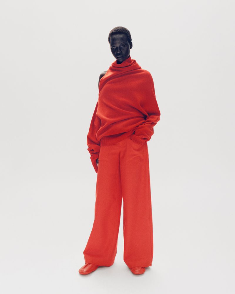 An adult fashion model with dark skin poses in a studio wearing a monochromatic red oversized sweater, wide-leg pants, and matching shoes.