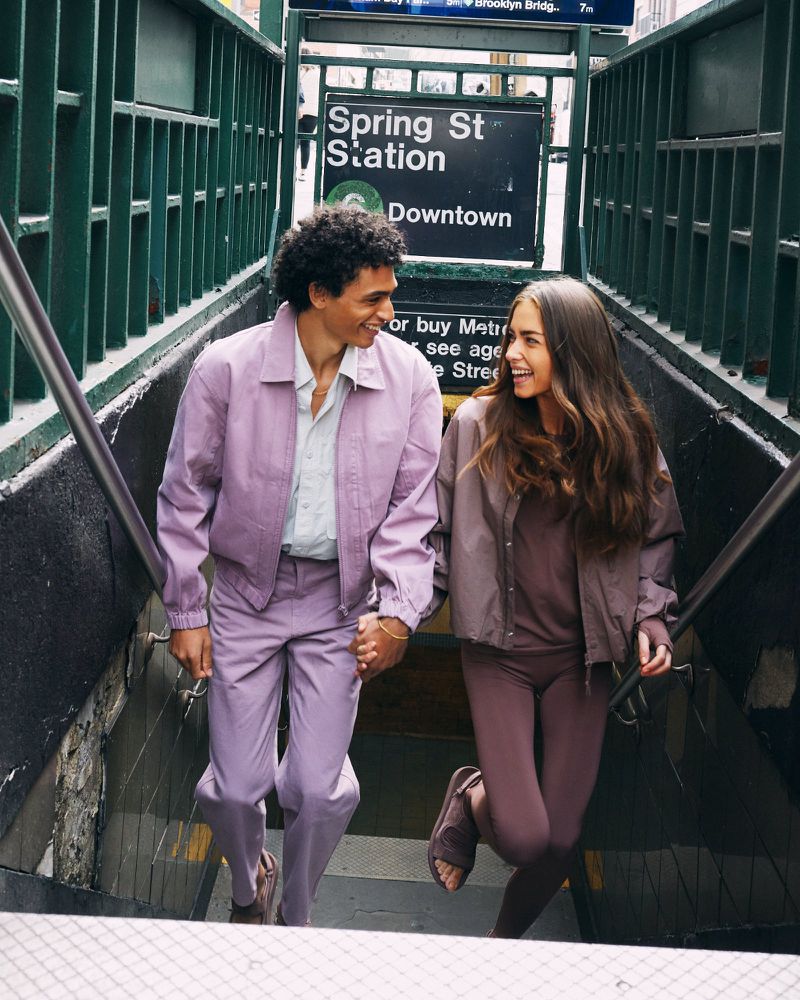 A stylish couple in matching outfits descends subway stairs, captured in medium shot, showcasing fashion and urban life with soft lighting.