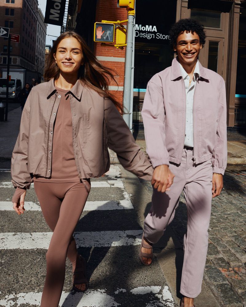 A happy couple wearing matching casual mauve outfits strolls hand-in-hand on a crosswalk with MoMA Design Store in the background.