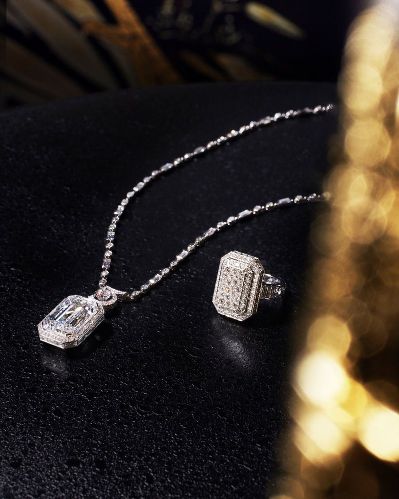 Elegant diamond jewelry set: pendant necklace with a matching ring, displayed against a dark background with a blurred gold element.